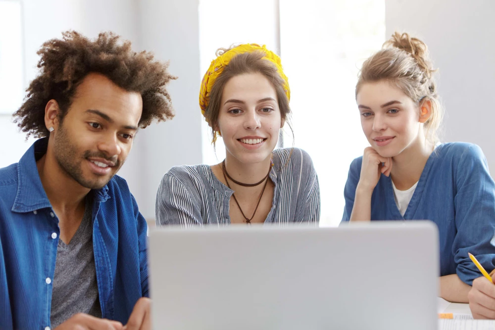 Drei Personen blicken gemeinsam auf einen Laptop